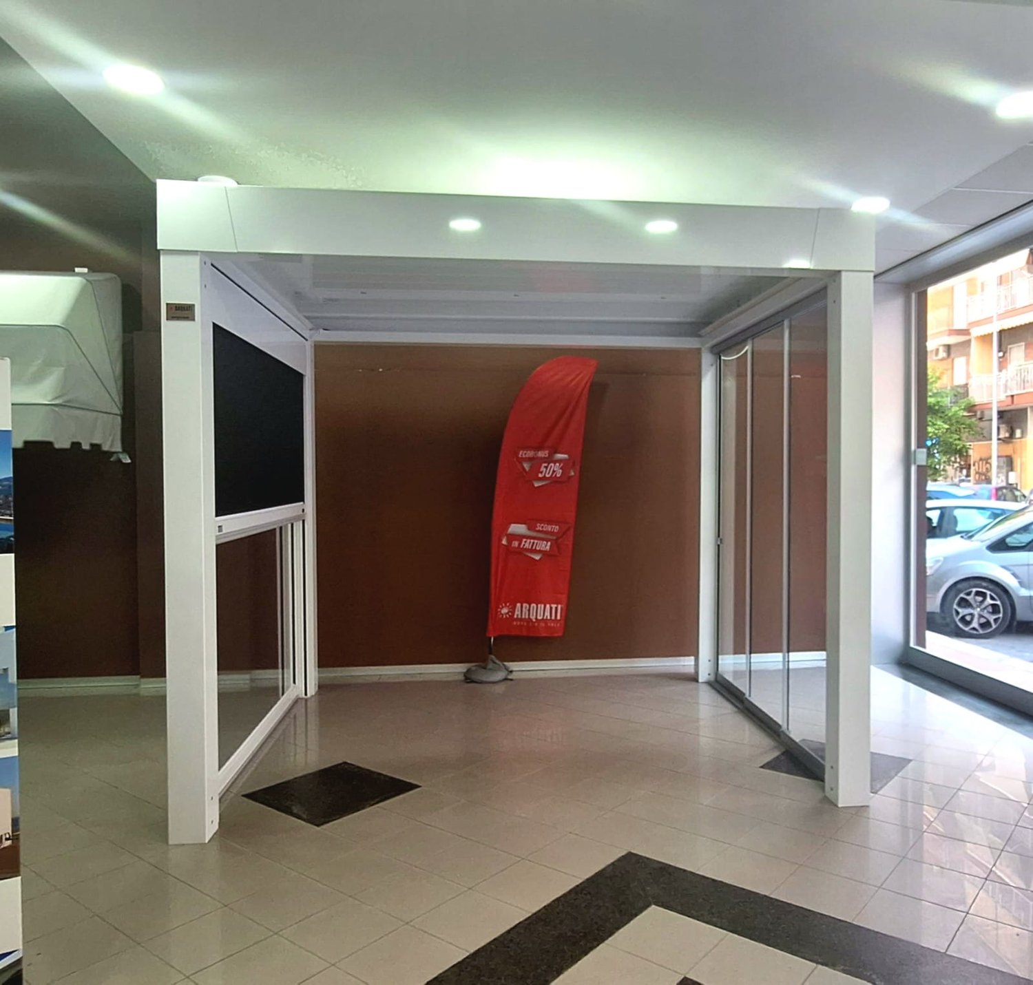 Pergola bianca con vetri scorrevoli nello showroom Sipi Color e bandiera rossa Arquati «Ecobonus 50% Sconto in fattura